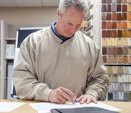 Person in a beige sweater sketching at a table in a studio with color swatches behind them