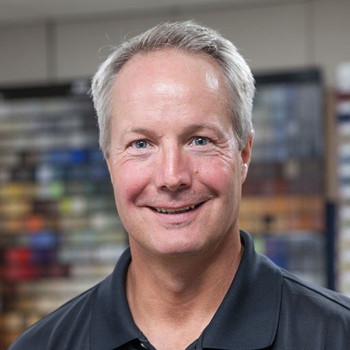 Smiling man in a dark polo shirt with blurred shelves in the background