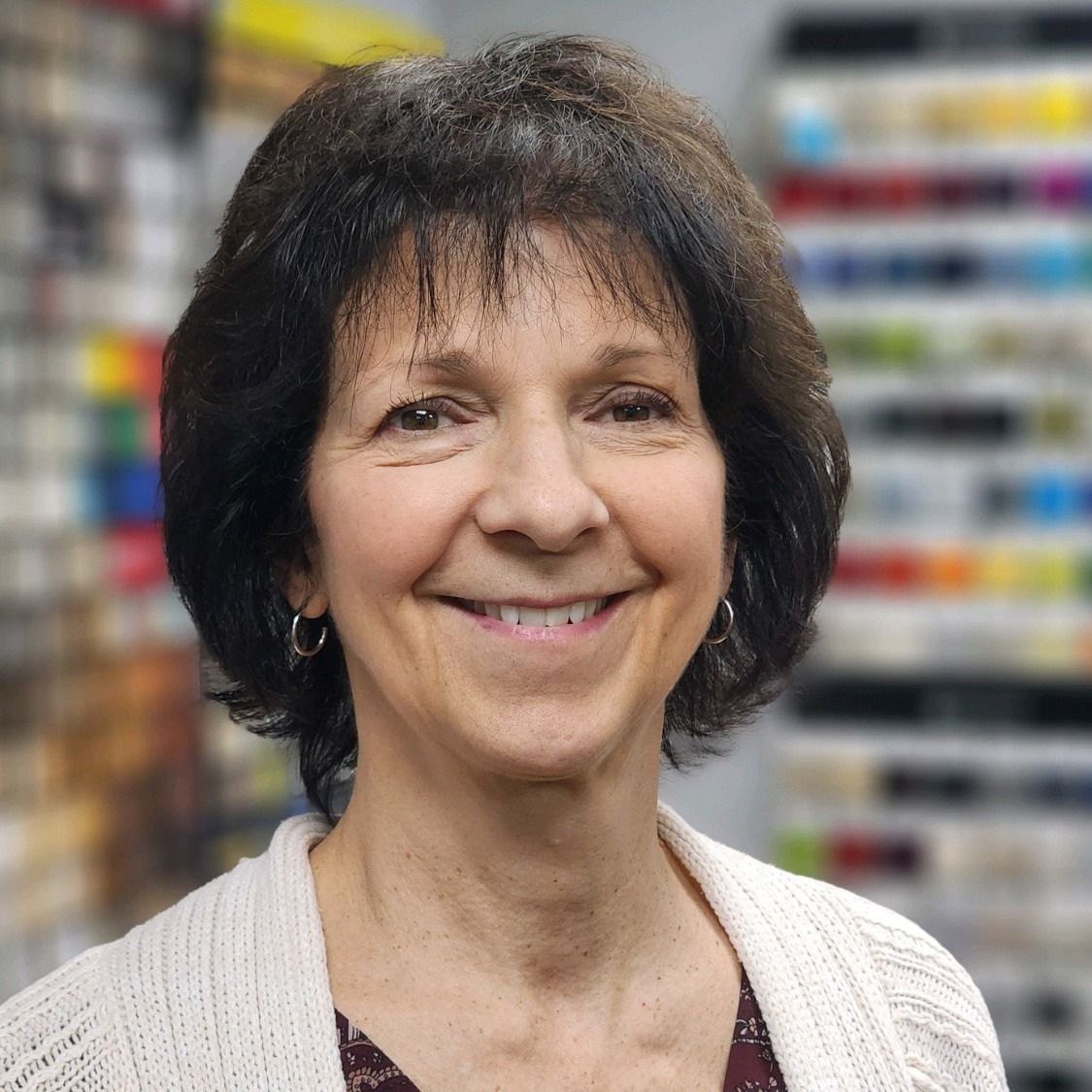 Smiling woman in a white sweater in front of blurred shelves of colorful spools