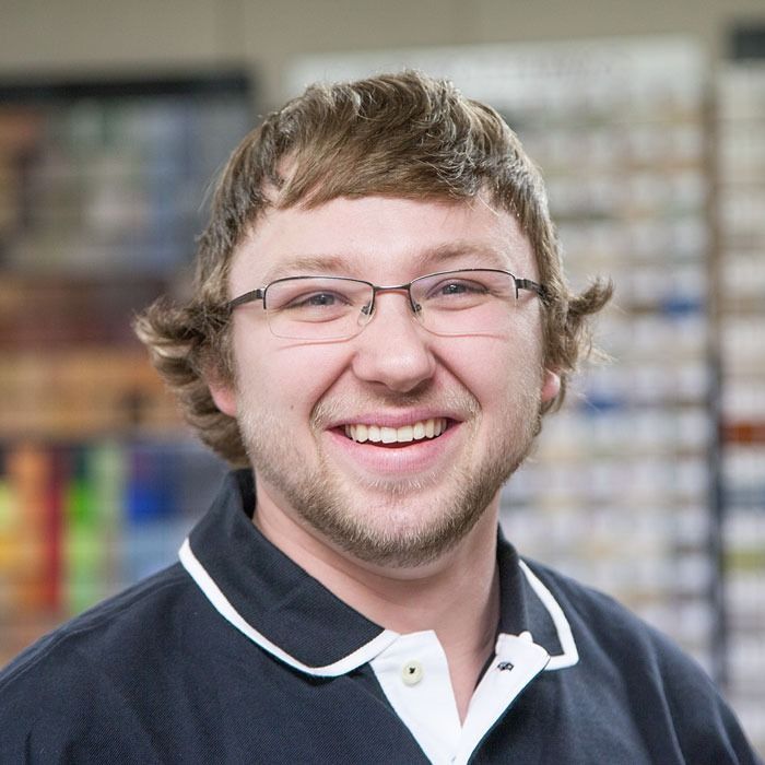 Smiling person wearing glasses and a navy polo shirt, standing in front of blurred shelves in a store.
