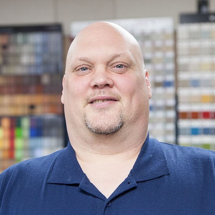Smiling bald man in a navy polo shirt standing in a store aisle with shelves in the background