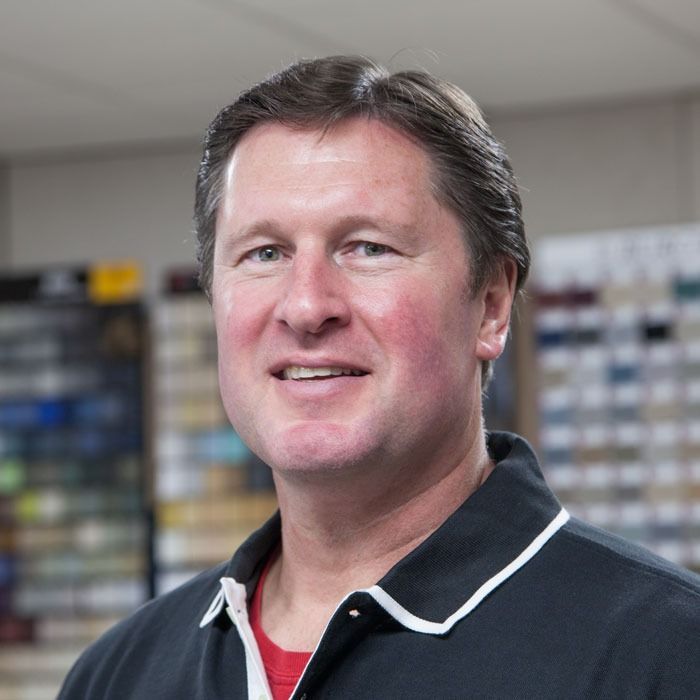 Smiling man in a dark polo shirt standing in a store aisle with blurred shelves behind him