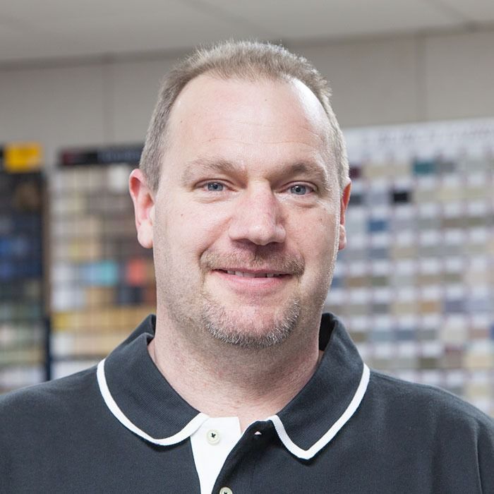 Smiling man in a black collared shirt standing indoors with shelves in the background