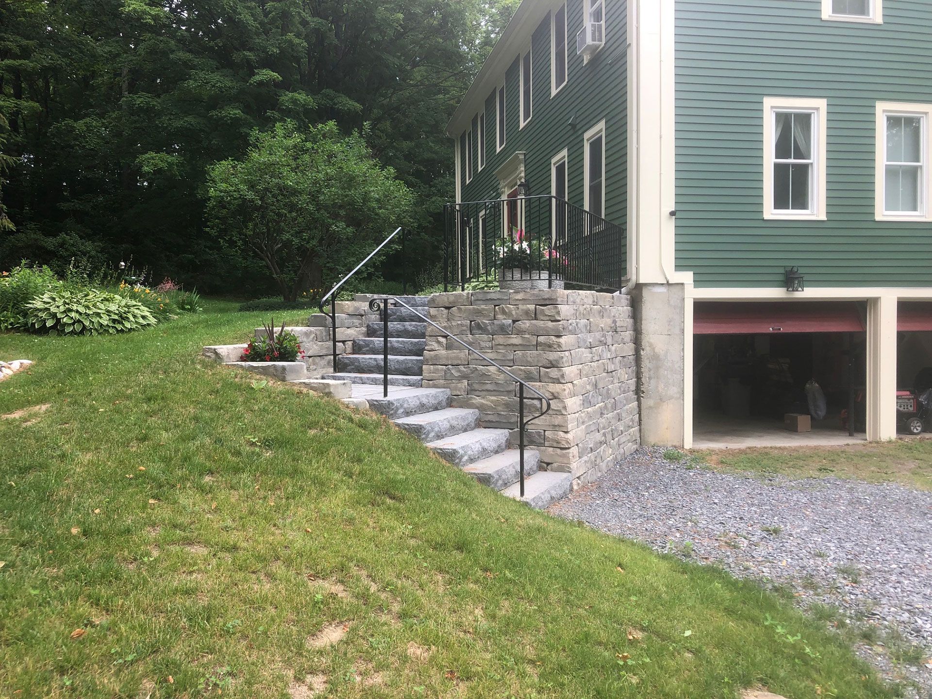 Stone steps with railings lead up to a green house with a garage.