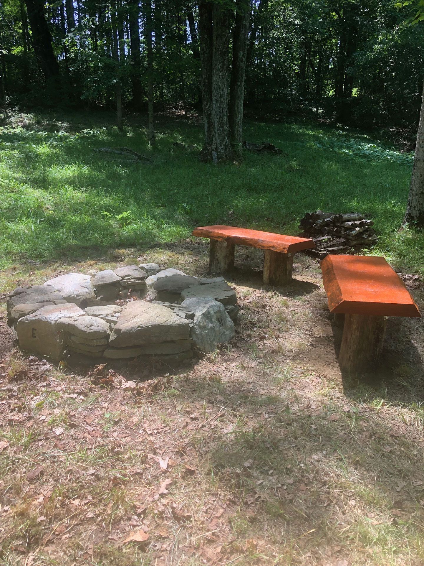 A fire pit with stone walls and two wooden benches in a wooded area.