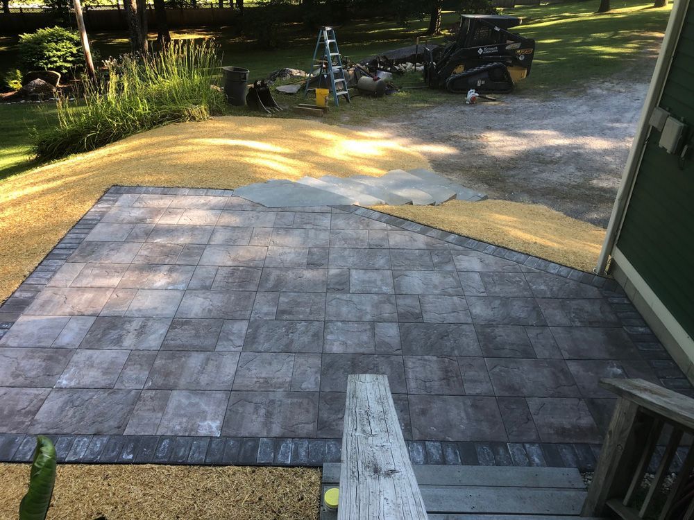 Finished brick patio next to a house with unfinished gravel and equipment in the background.