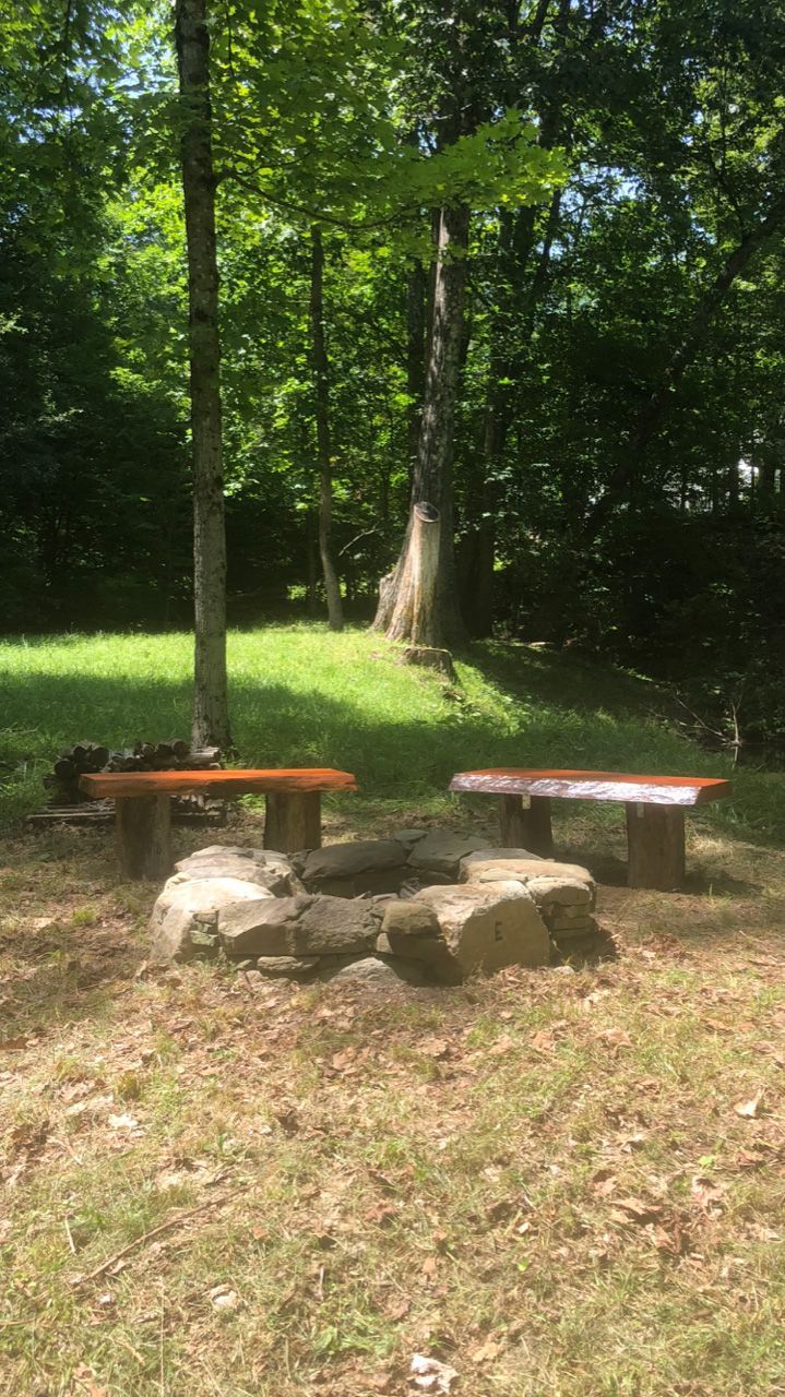 A campfire ring with two wooden benches in a wooded area on a sunny day.