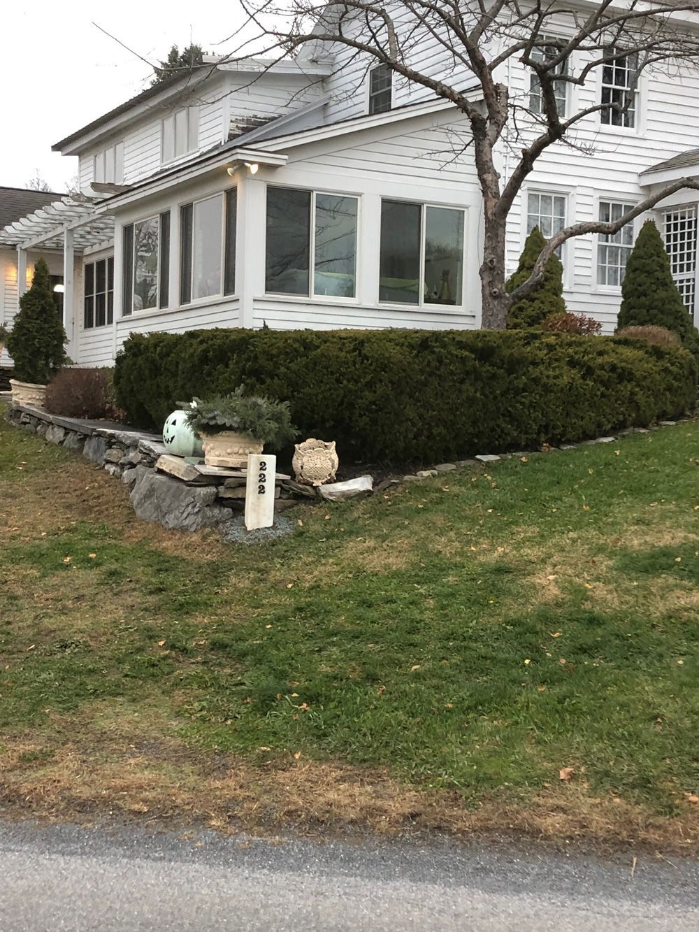 White house with a green lawn, shrubs, and a rock wall. A few decorative objects are in the garden.