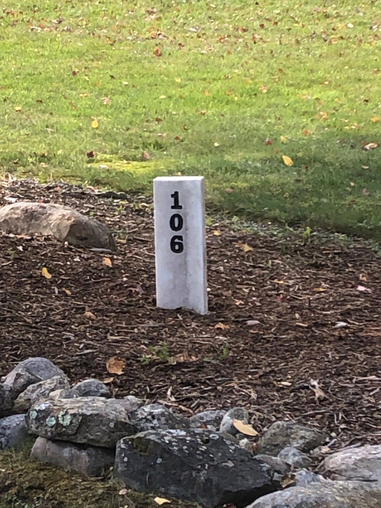 Stone marker with the number 106 in a garden bed.