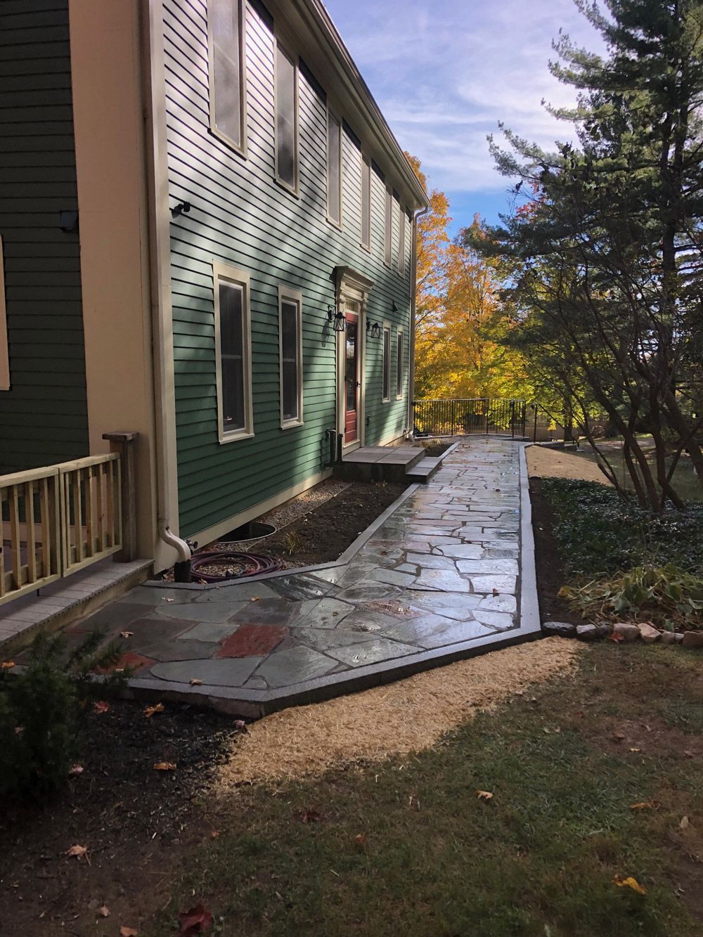 Exterior view of a green house with a flagstone pathway leading to the entrance. Fall foliage in the background.