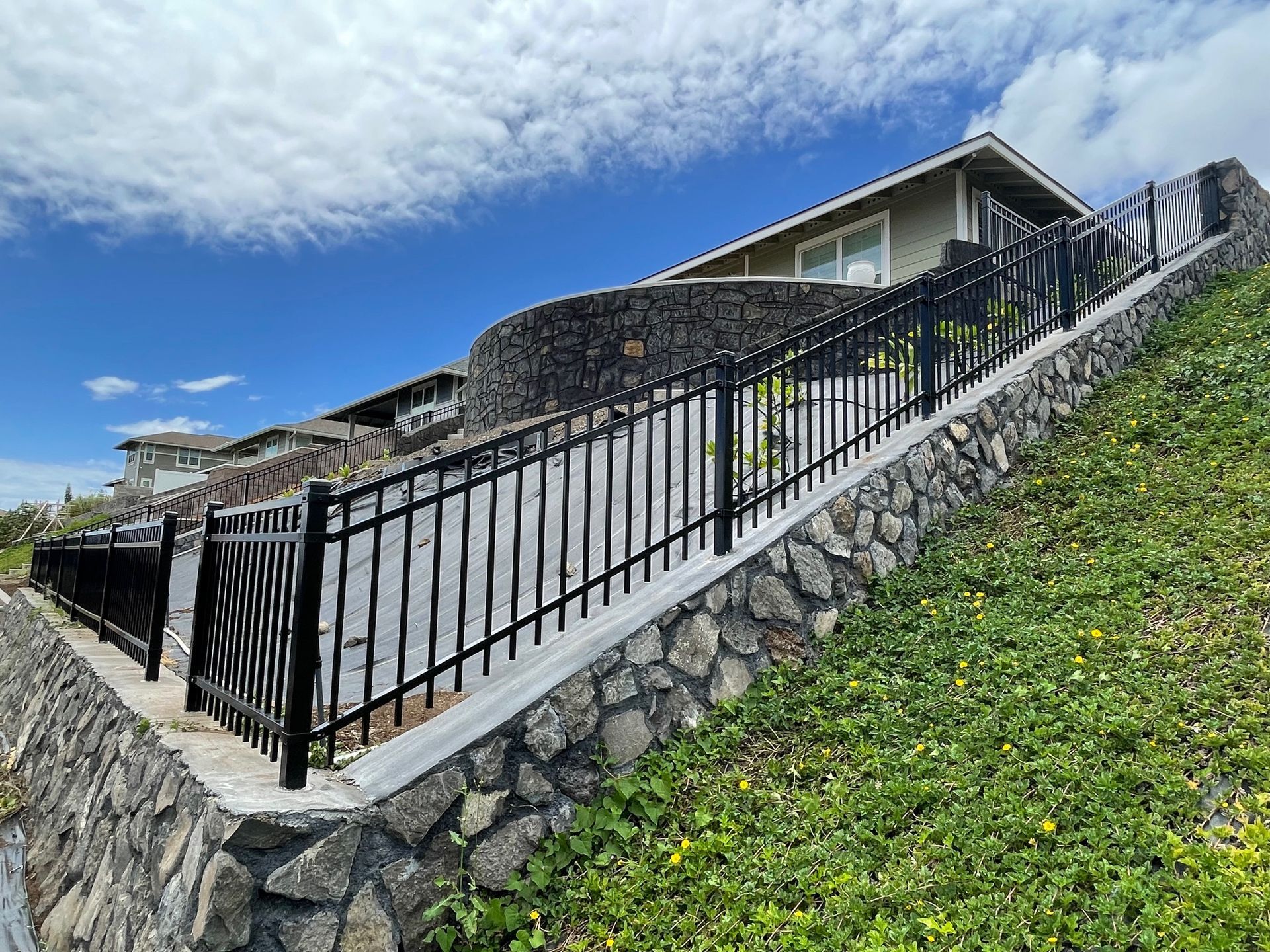 A house with a stone wall and a metal fence surrounding it.