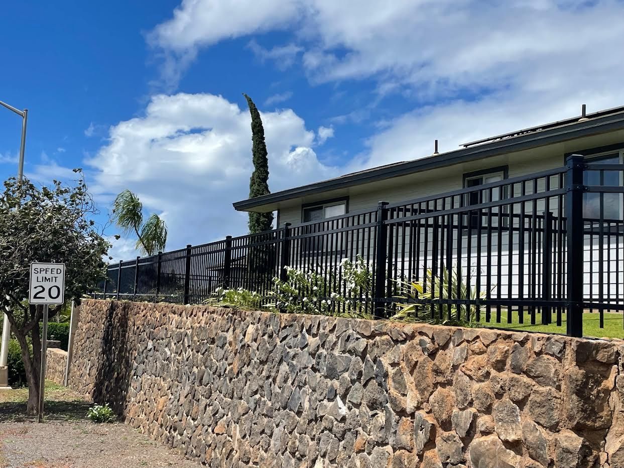 A stone wall surrounds a house with a metal fence.