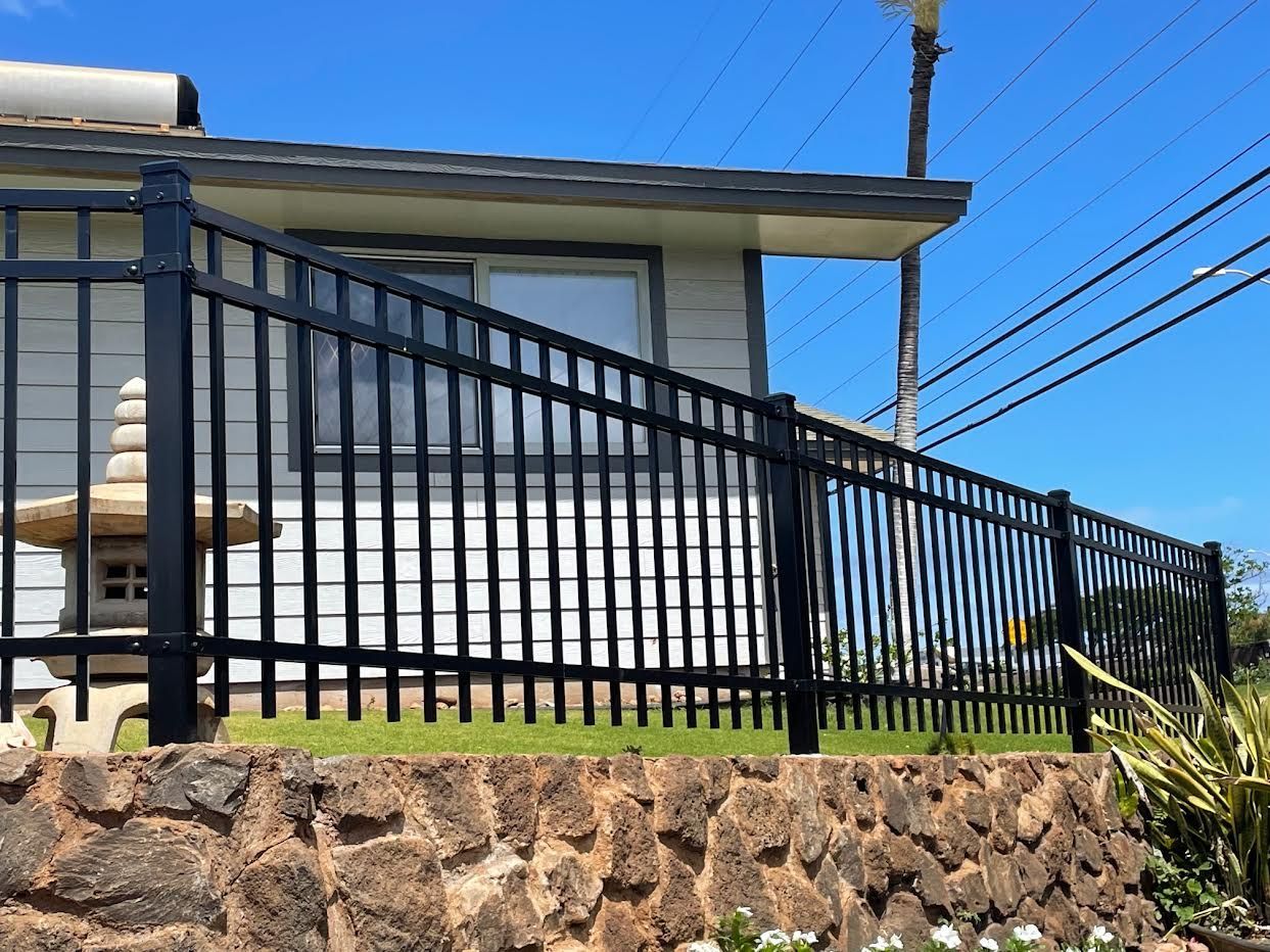 A black fence is surrounding a house with a stone wall.