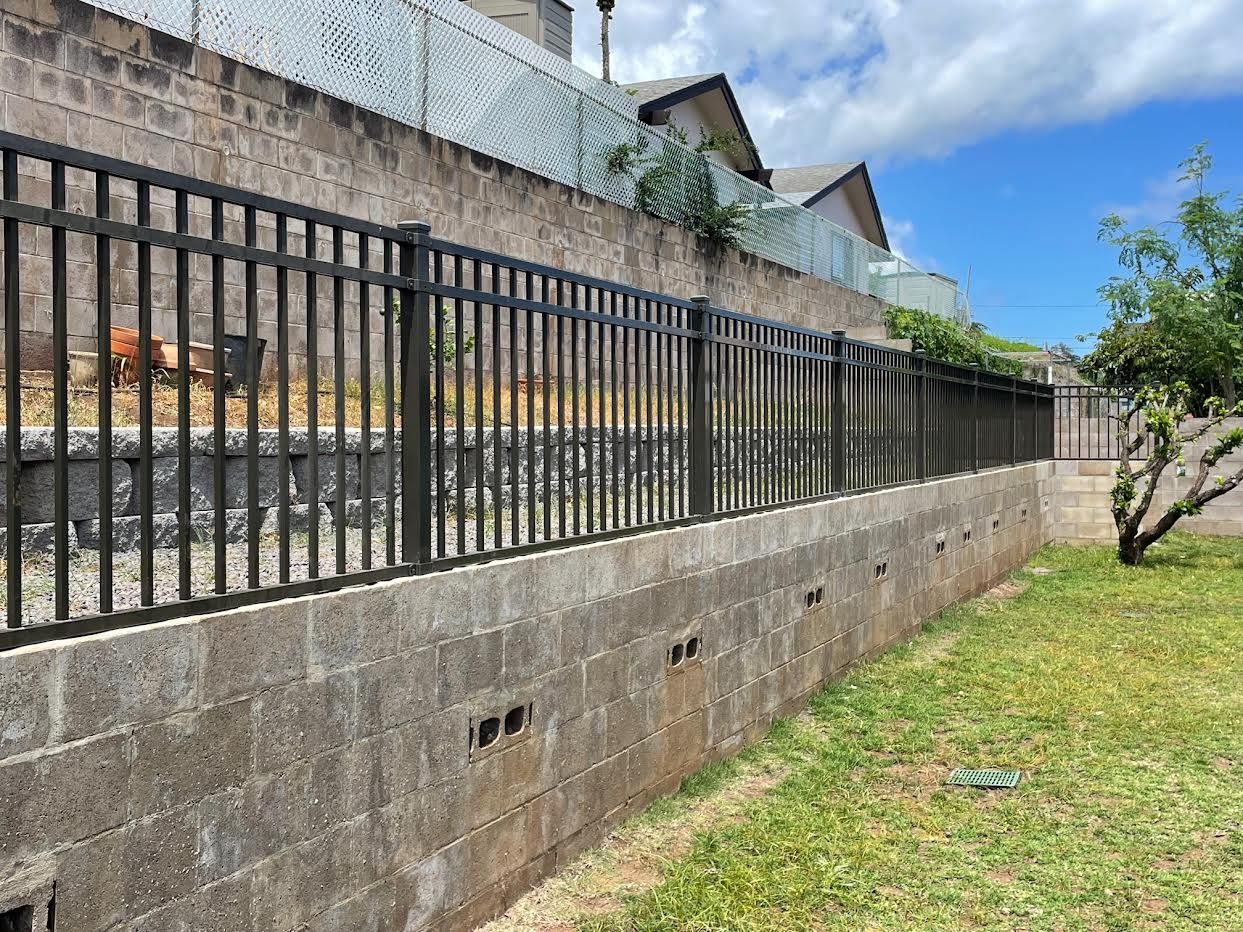 A metal fence surrounds a brick wall in a backyard.