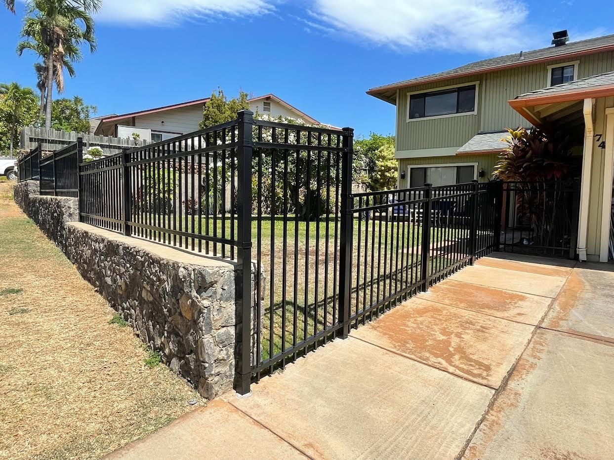 A black metal fence surrounds a house with a stone wall.