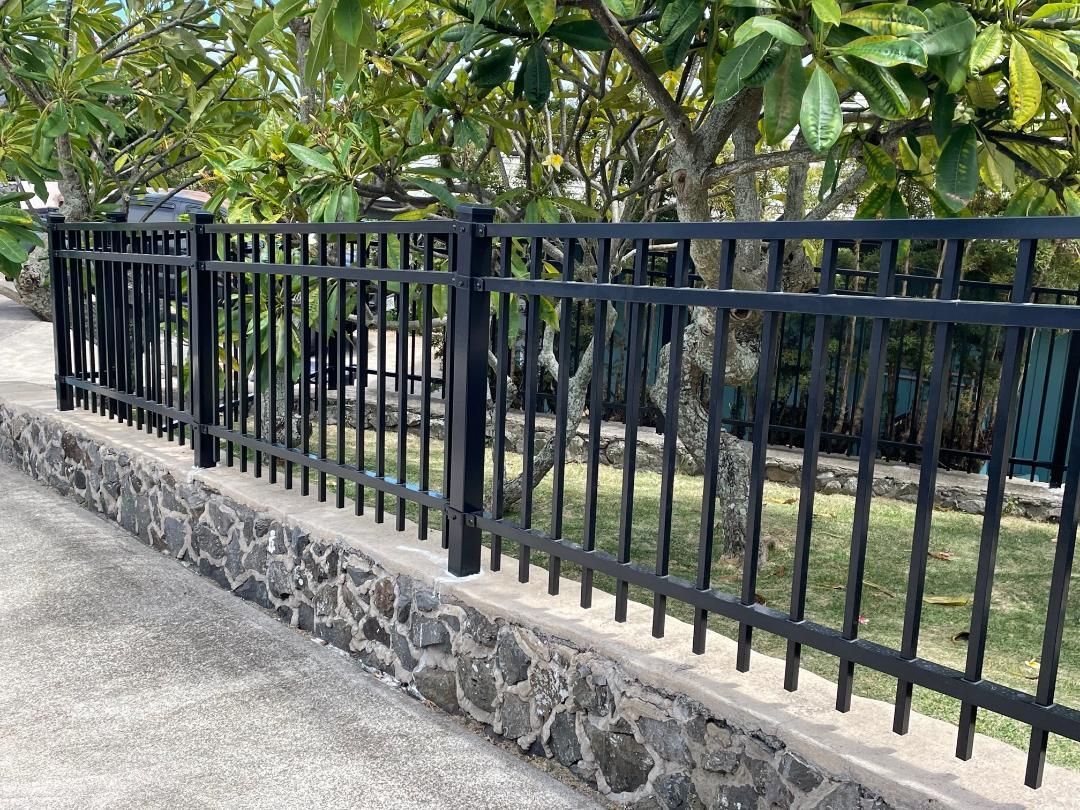 A black metal fence is surrounding a stone wall.