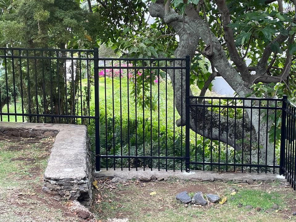 A black metal fence with a stone wall and a tree in the background.