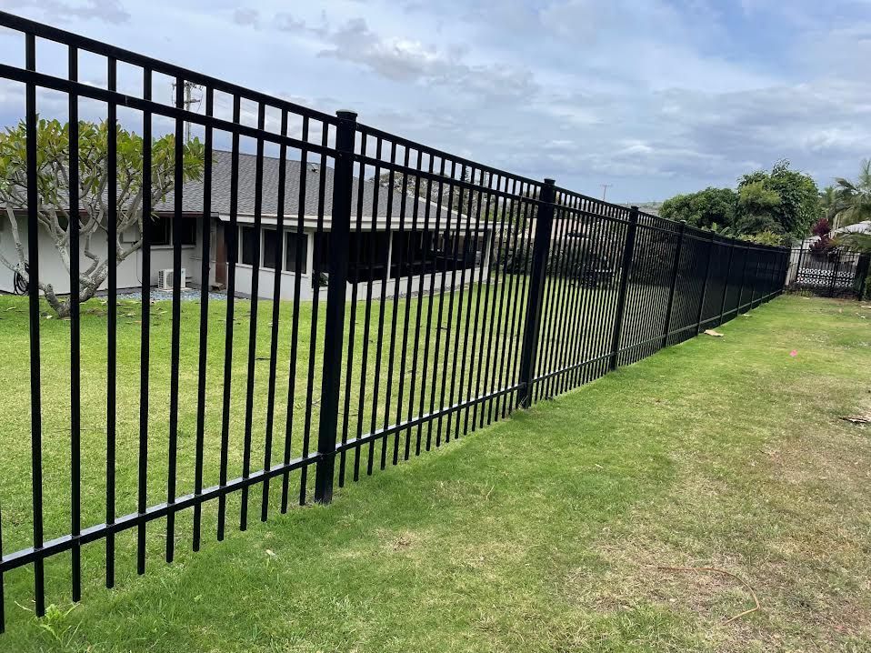 A black metal fence surrounds a lush green yard in front of a house.