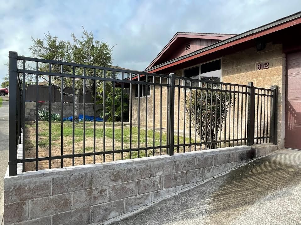 A black fence is surrounding a brick wall in front of a house.