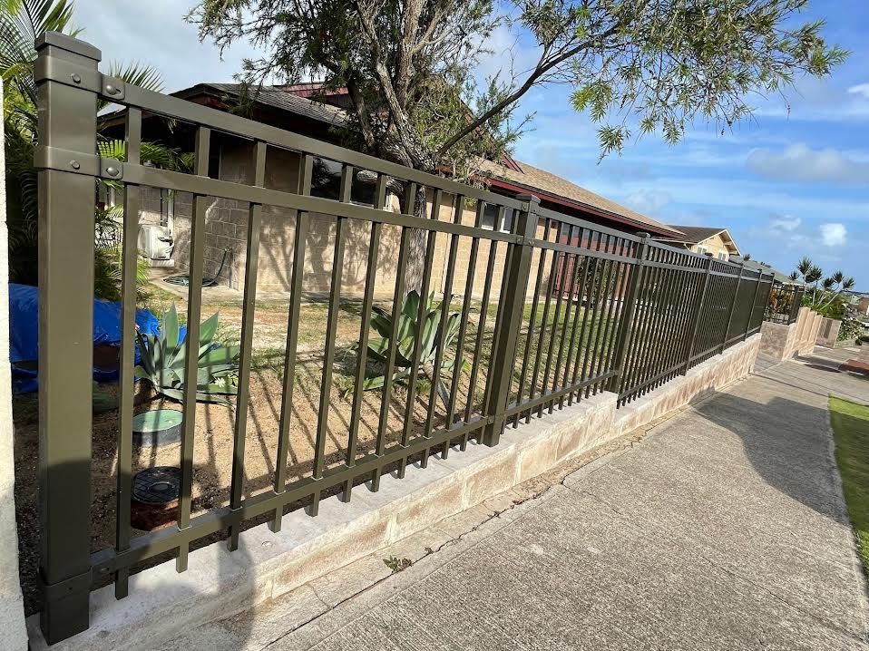A metal fence surrounds a stone wall in front of a house.