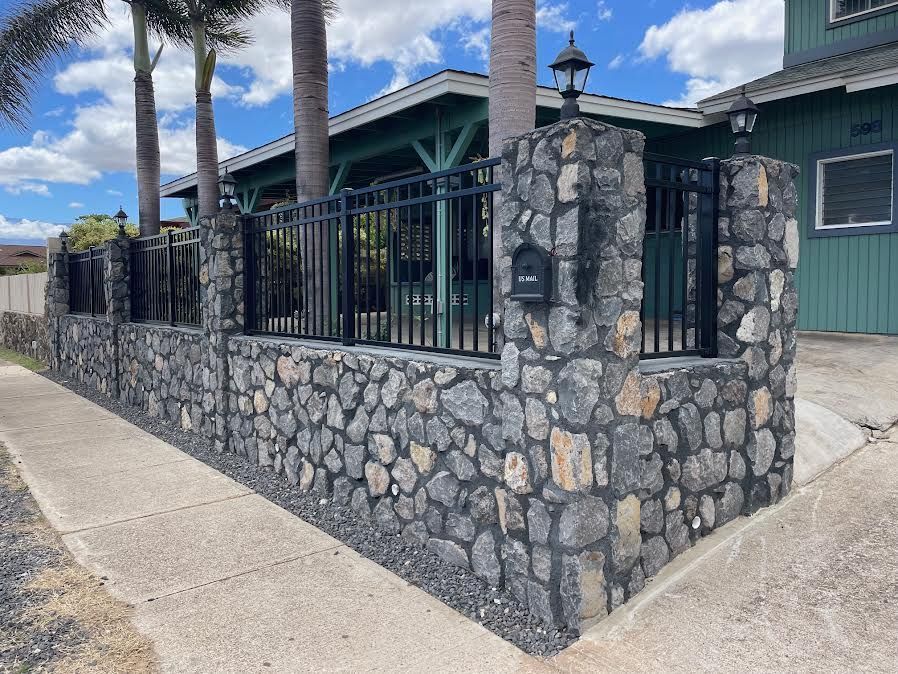 A stone wall with a metal fence and a mailbox in front of a house.