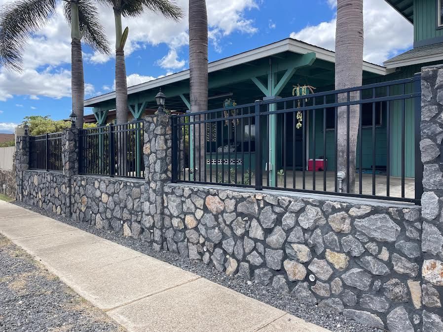 A stone wall with a metal fence in front of a house.