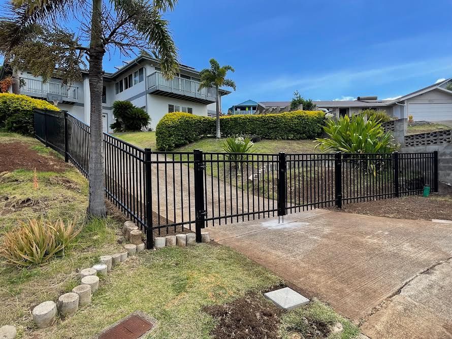 A black fence surrounds a driveway in front of a house.