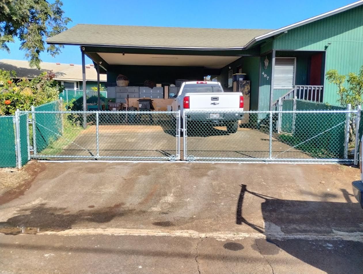 A white truck is parked in front of a green house behind a chain link fence.