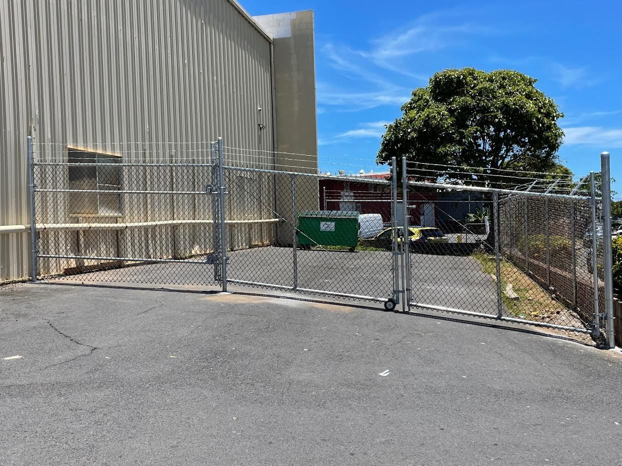 A chain link fence surrounds a parking lot in front of a building.