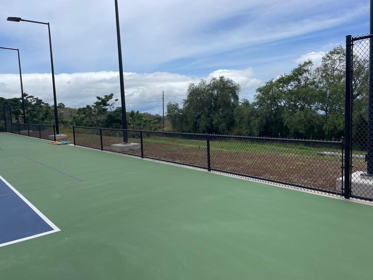 A tennis court with a fence around it and trees in the background.