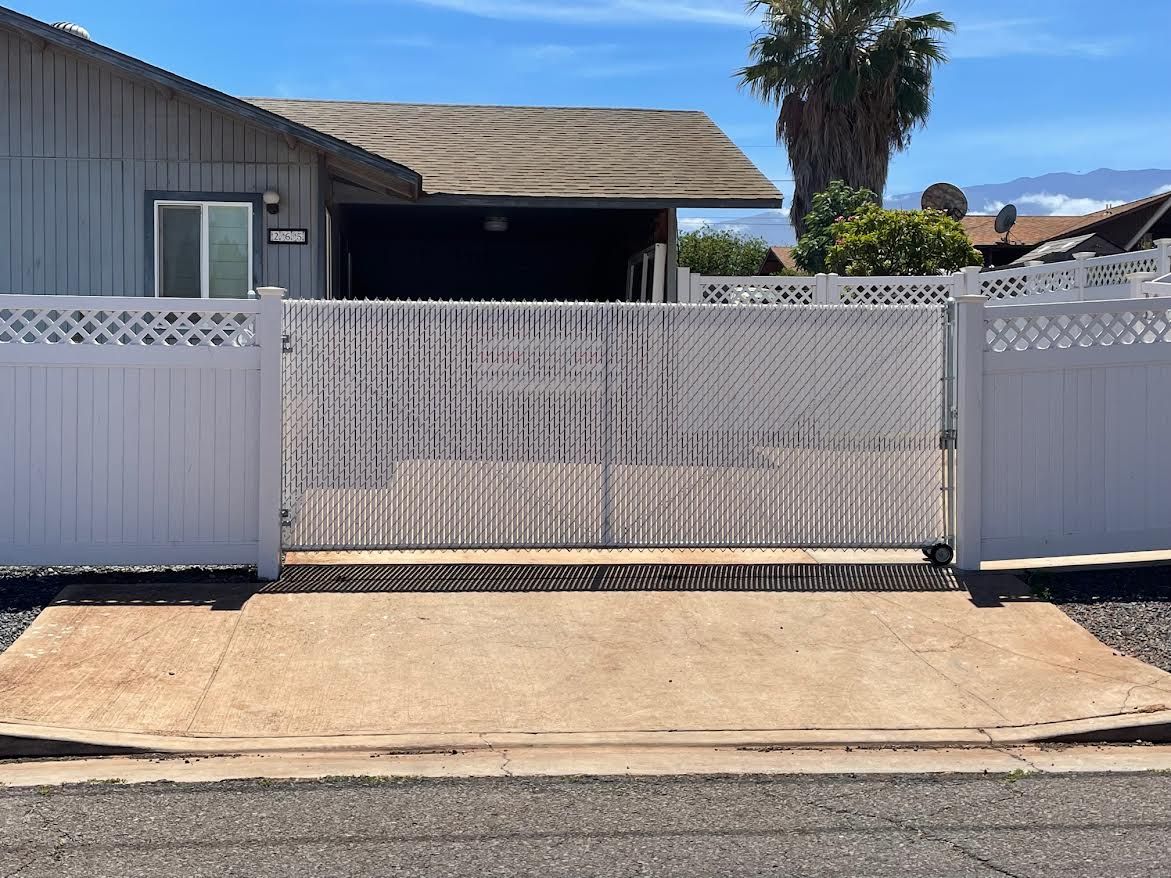 A white fence surrounds a driveway in front of a house.