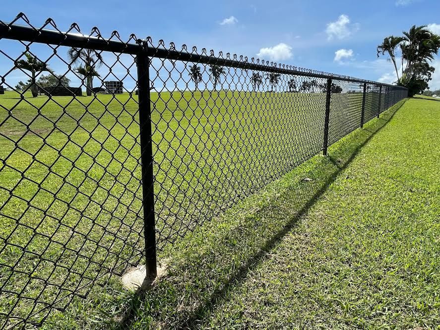A chain link fence surrounds a lush green field.