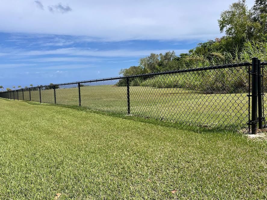 A chain link fence surrounds a grassy field with a view of the ocean.