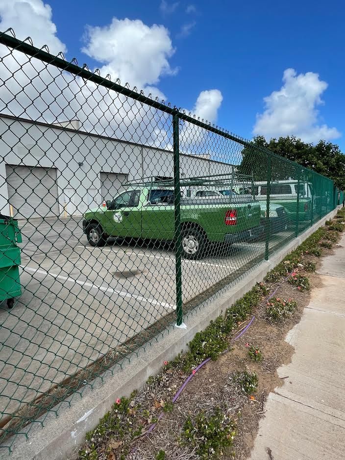 A green truck is parked behind a chain link fence.