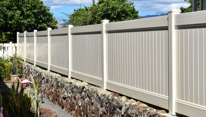 A white fence is sitting next to a stone wall.