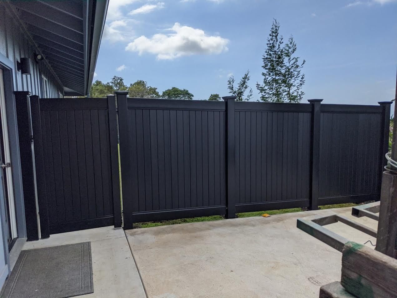A black fence is sitting on top of a concrete patio next to a house.
