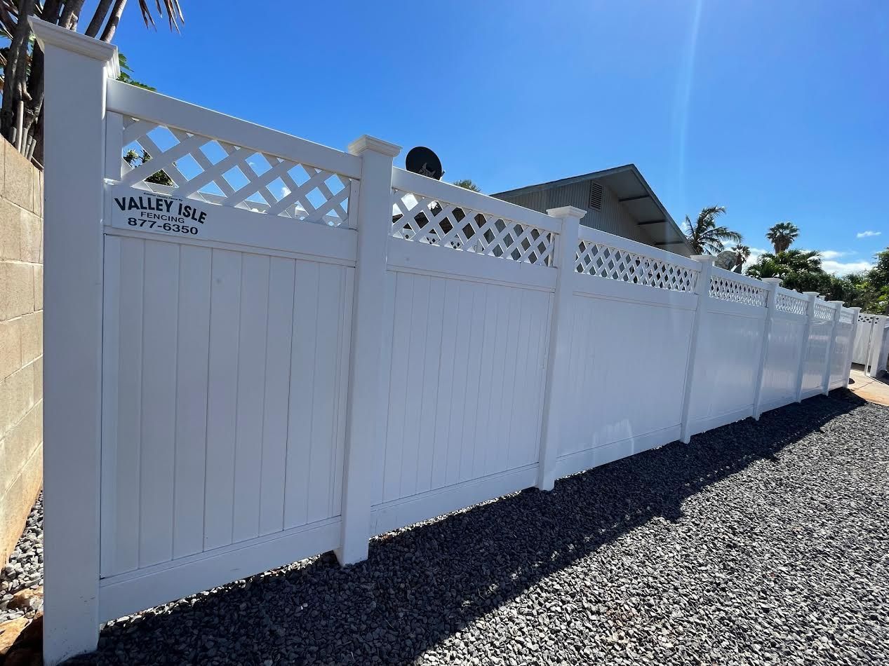 A white fence is sitting on top of a gravel driveway next to a house.