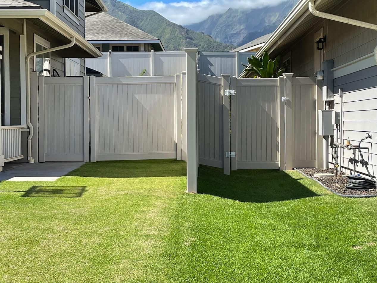 A white fence surrounds a lush green yard in front of a house with mountains in the background.