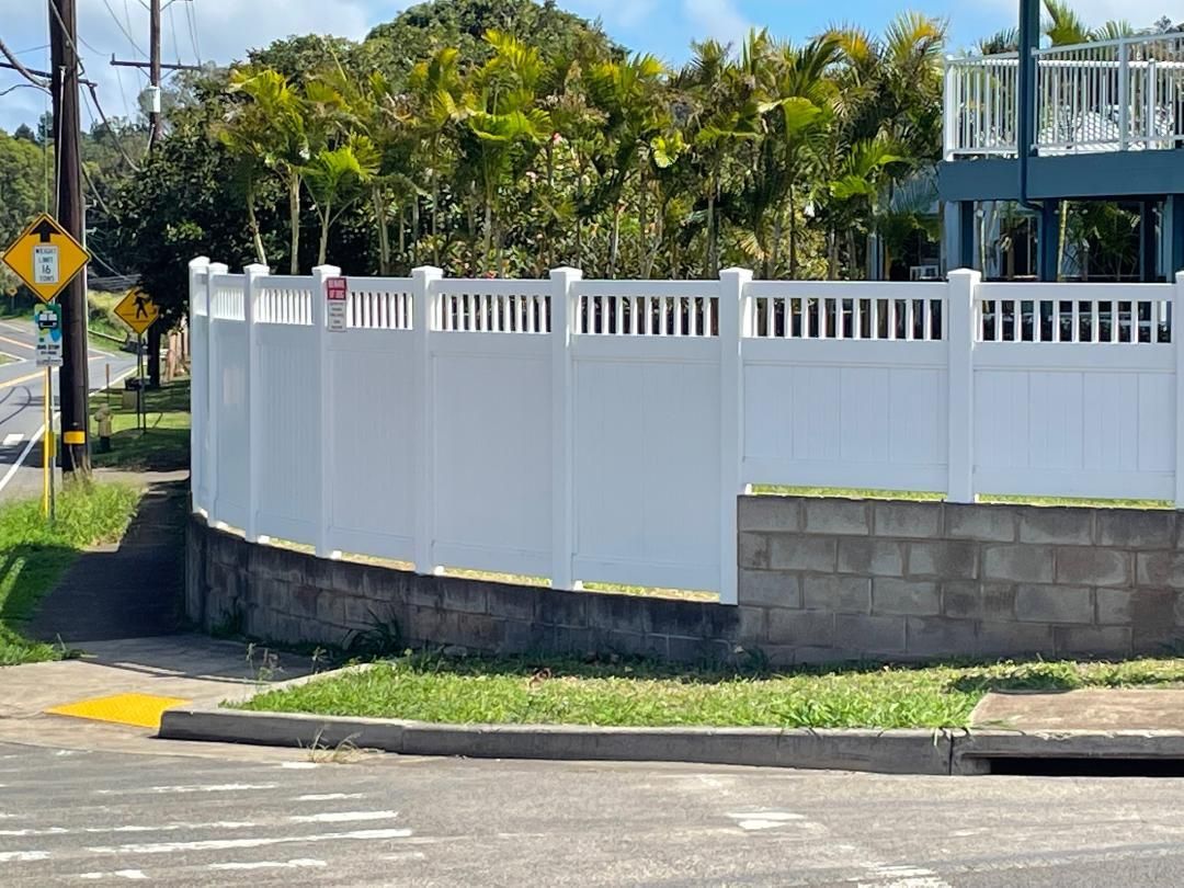A white fence is surrounding a brick wall on the side of a road.