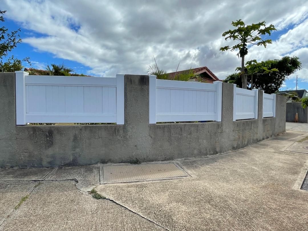 A white fence is sitting on top of a concrete wall.
