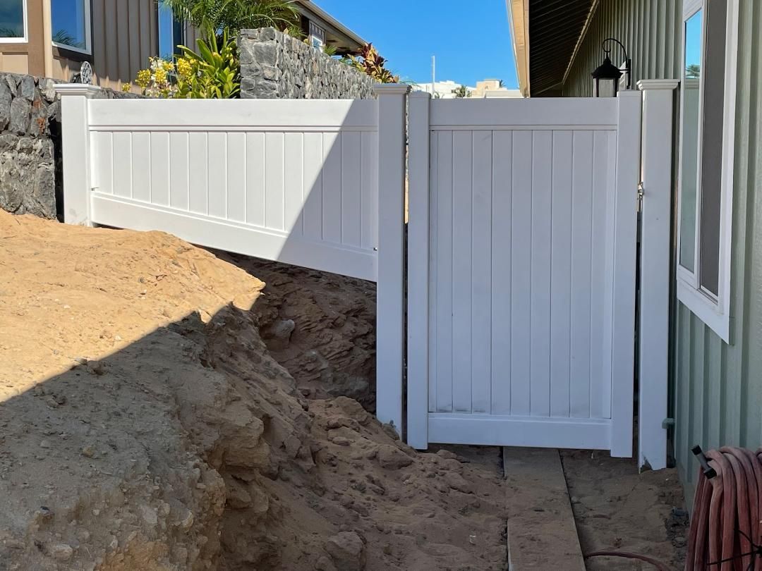 A white fence is sitting on top of a dirt hill next to a house.