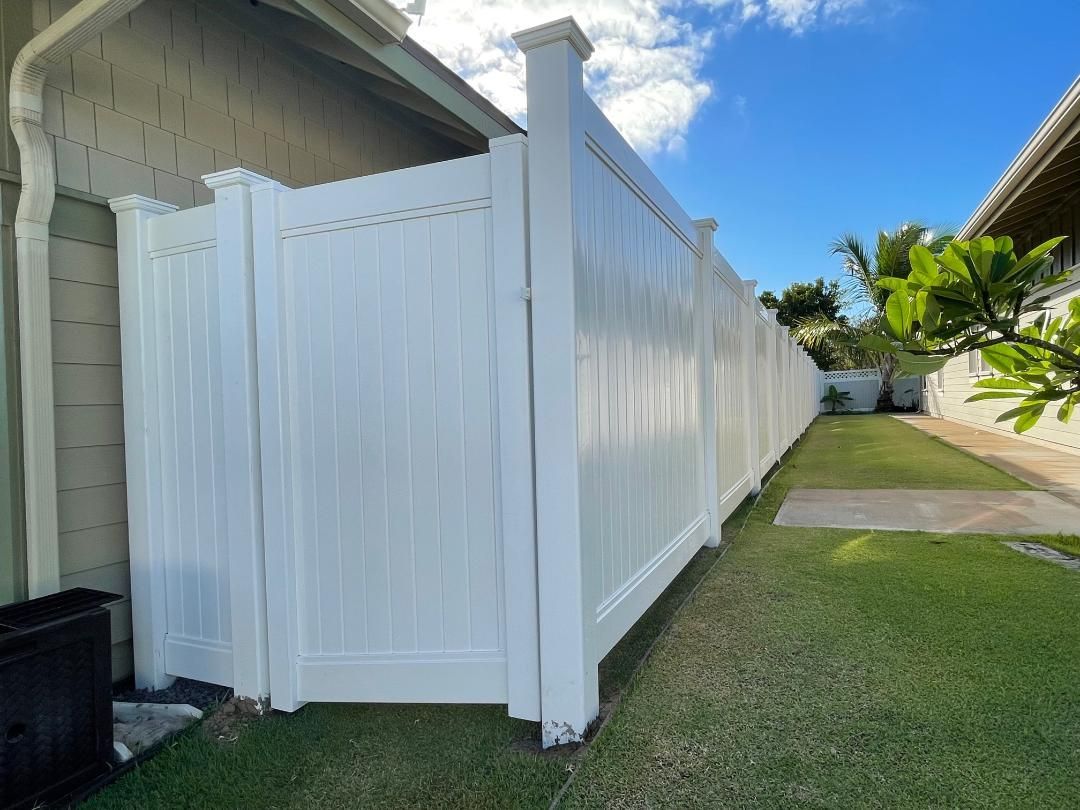 A white fence is sitting next to a house in a backyard.