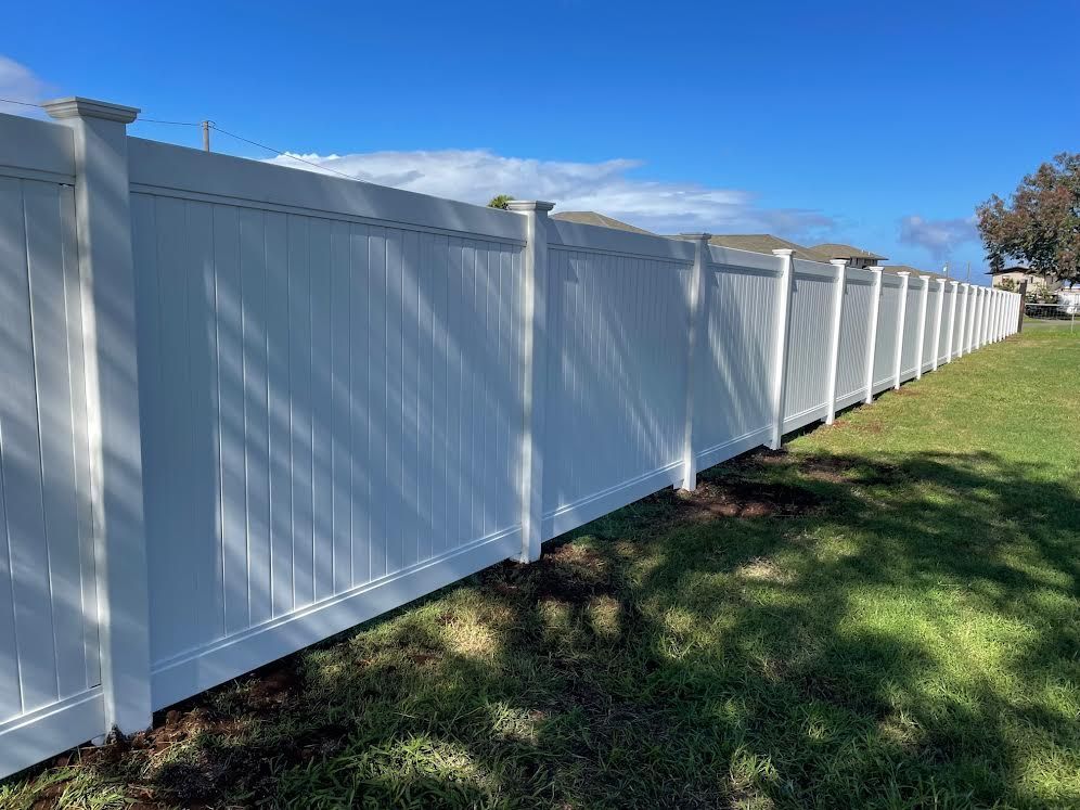 A white vinyl fence is sitting in the middle of a lush green field.