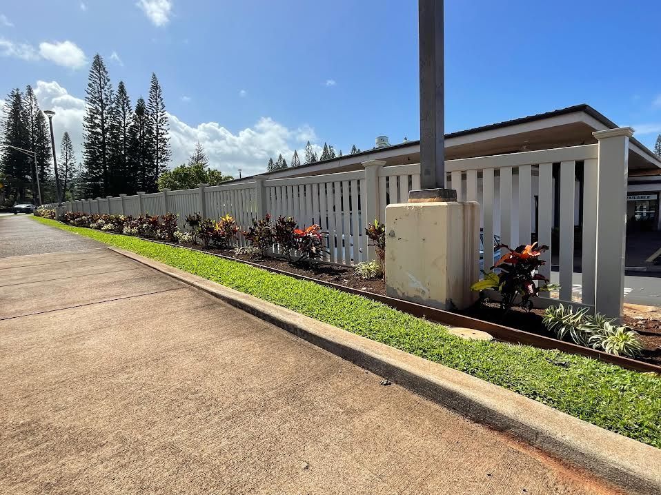 A white fence surrounds a parking lot with trees in the background