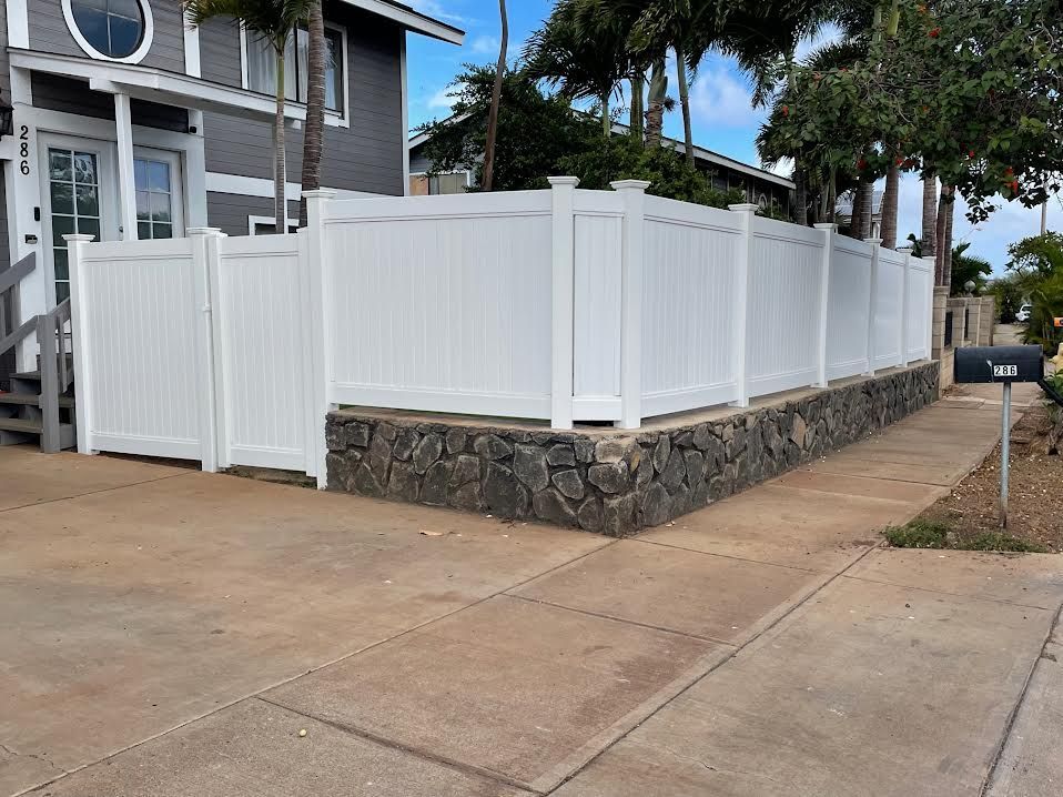 A white fence is surrounding a stone wall in front of a house.