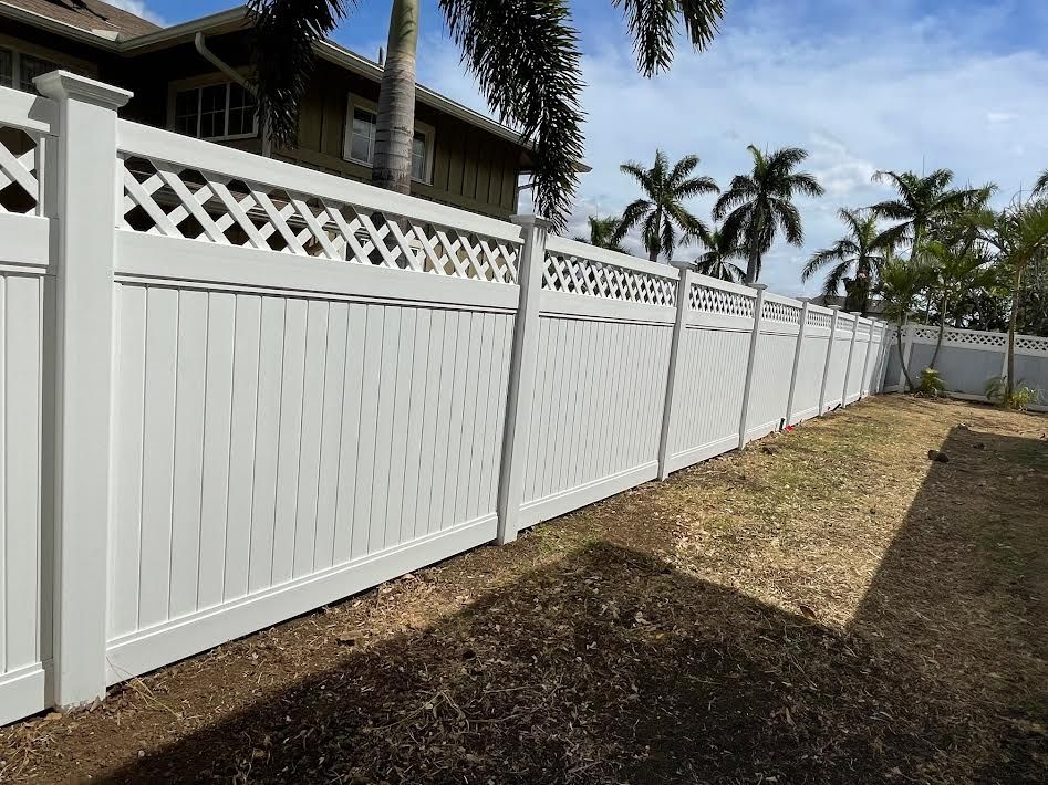 A white fence is in the backyard of a house with palm trees in the background.