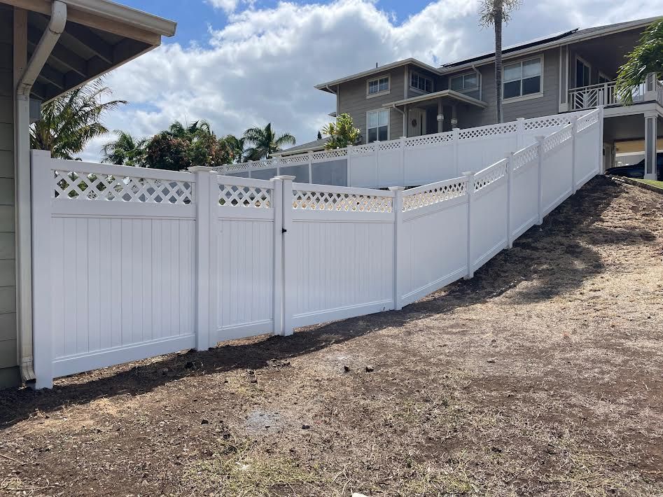 A white fence is sitting on top of a dirt hill next to a house.