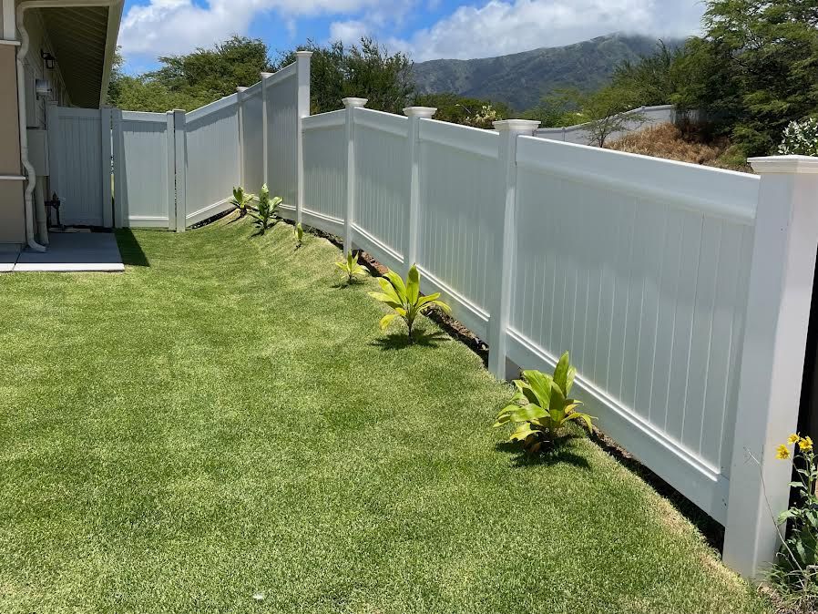 A white fence surrounds a lush green lawn in front of a house.