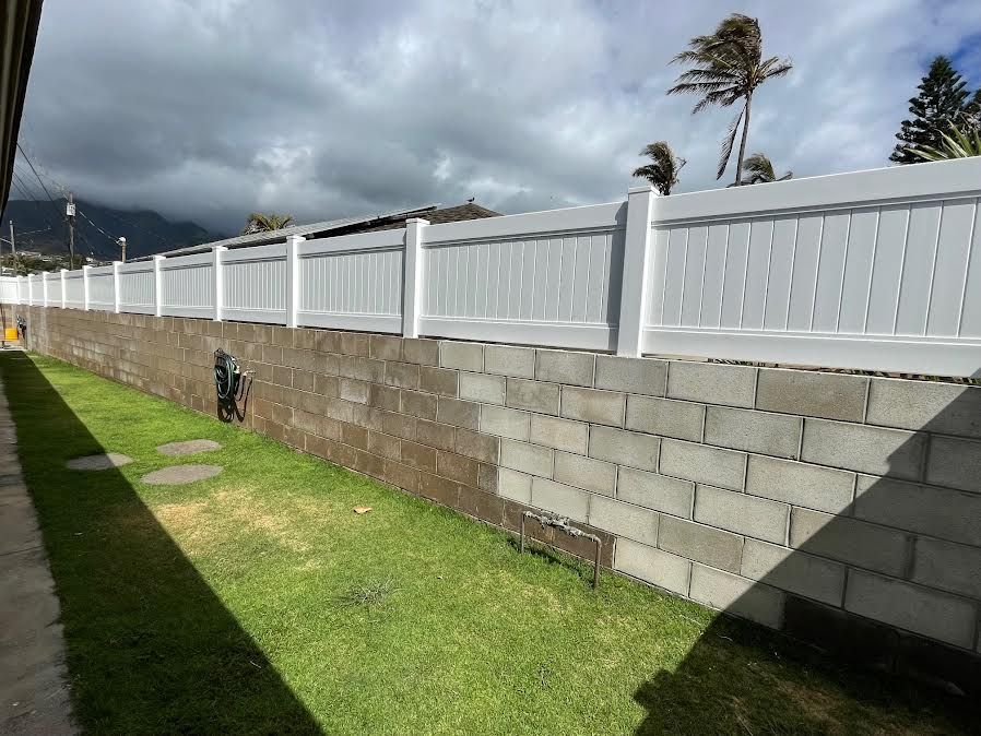 A white fence surrounds a brick wall in a backyard.