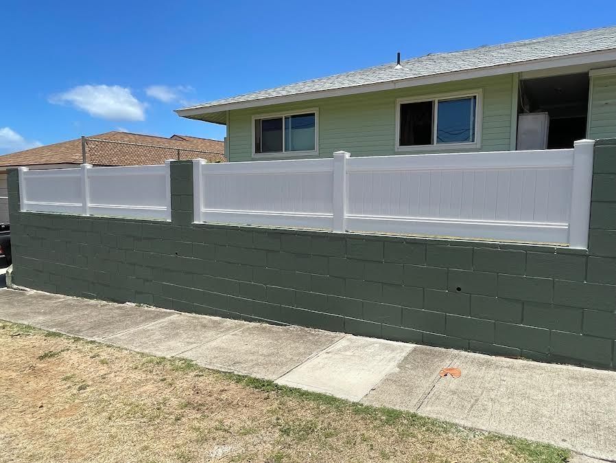A white fence is surrounding a brick wall in front of a house.